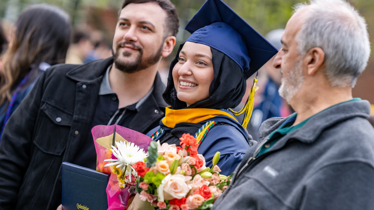 A graduate holds dozens of photos and poses for a photo with her guests