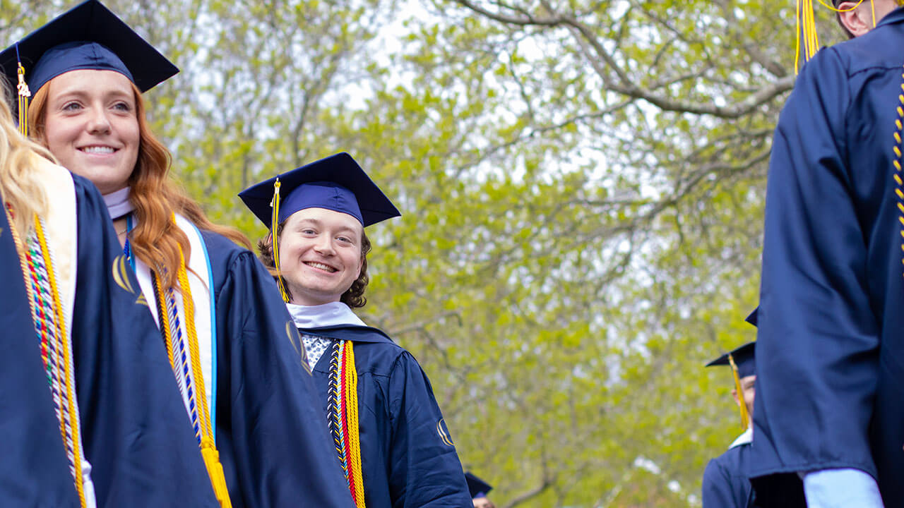 A graduate leans to the side and smiles as he walks in a line of graduates