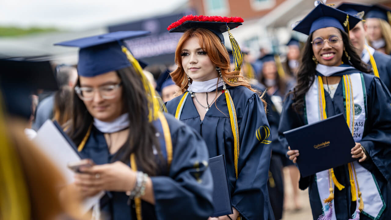 Several graduates with decorated caps walk in front of the library clocktower