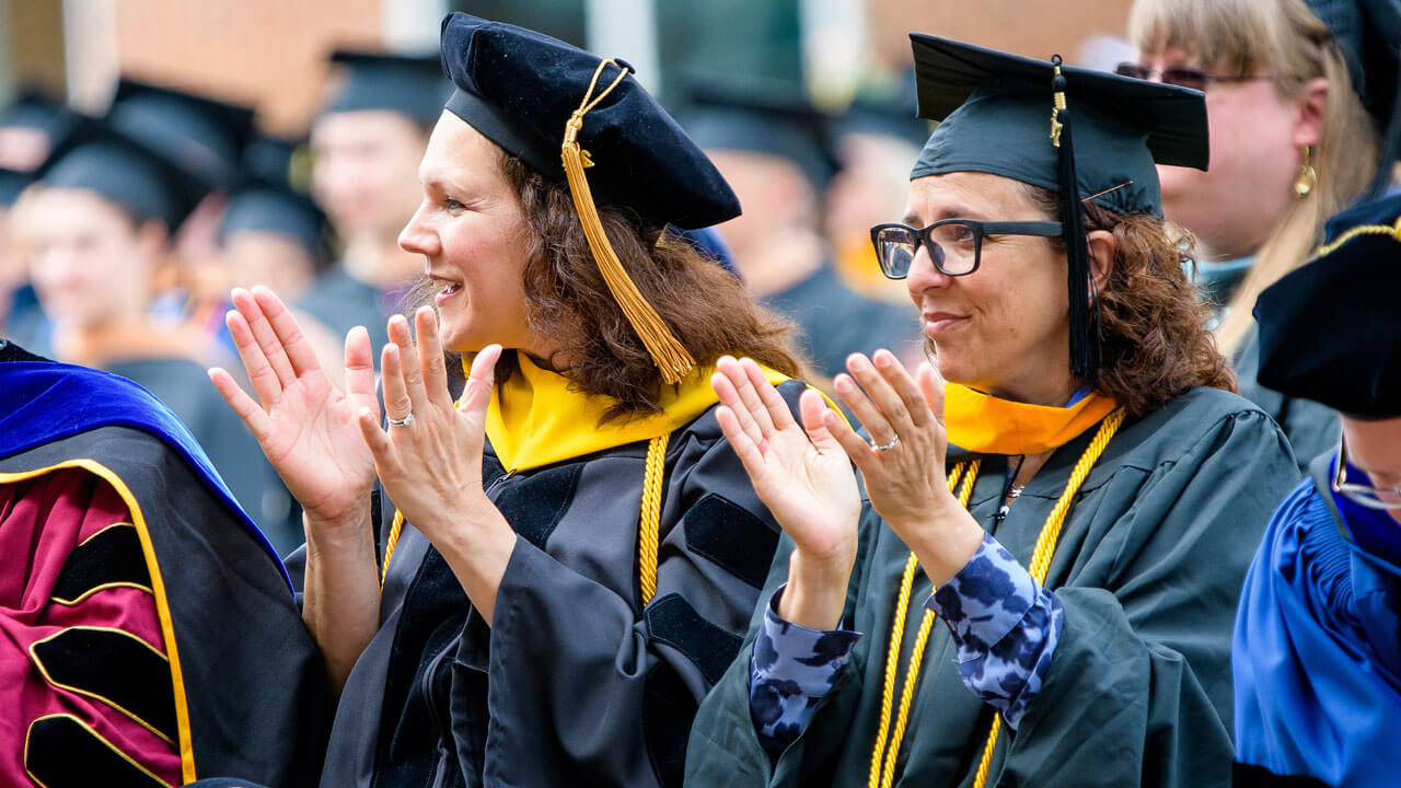 Two graduates clap while standing during the ceremony