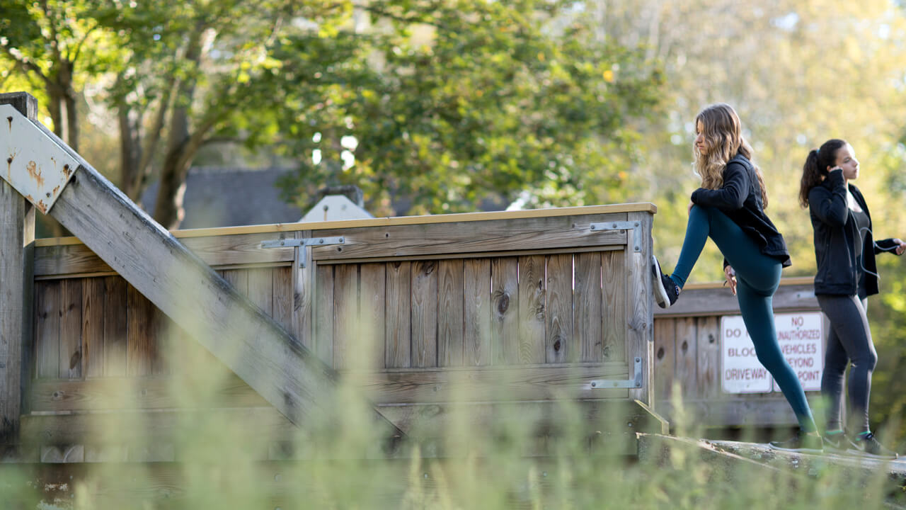 Two students stretch on a wooden bridge on a fall day