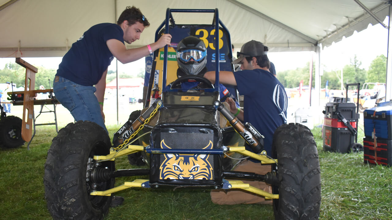 2 students inspecting the baja vehicle with the driver in it