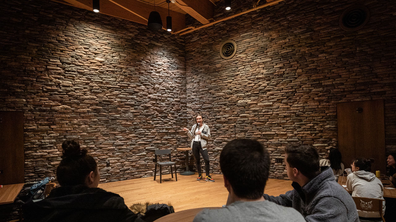 A student stands on the stage in the pub talking to an audience