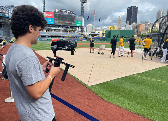 A student films at a baseball stadium.