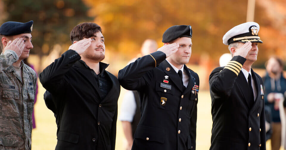 Students and staff in military uniforms stand in a line and salute